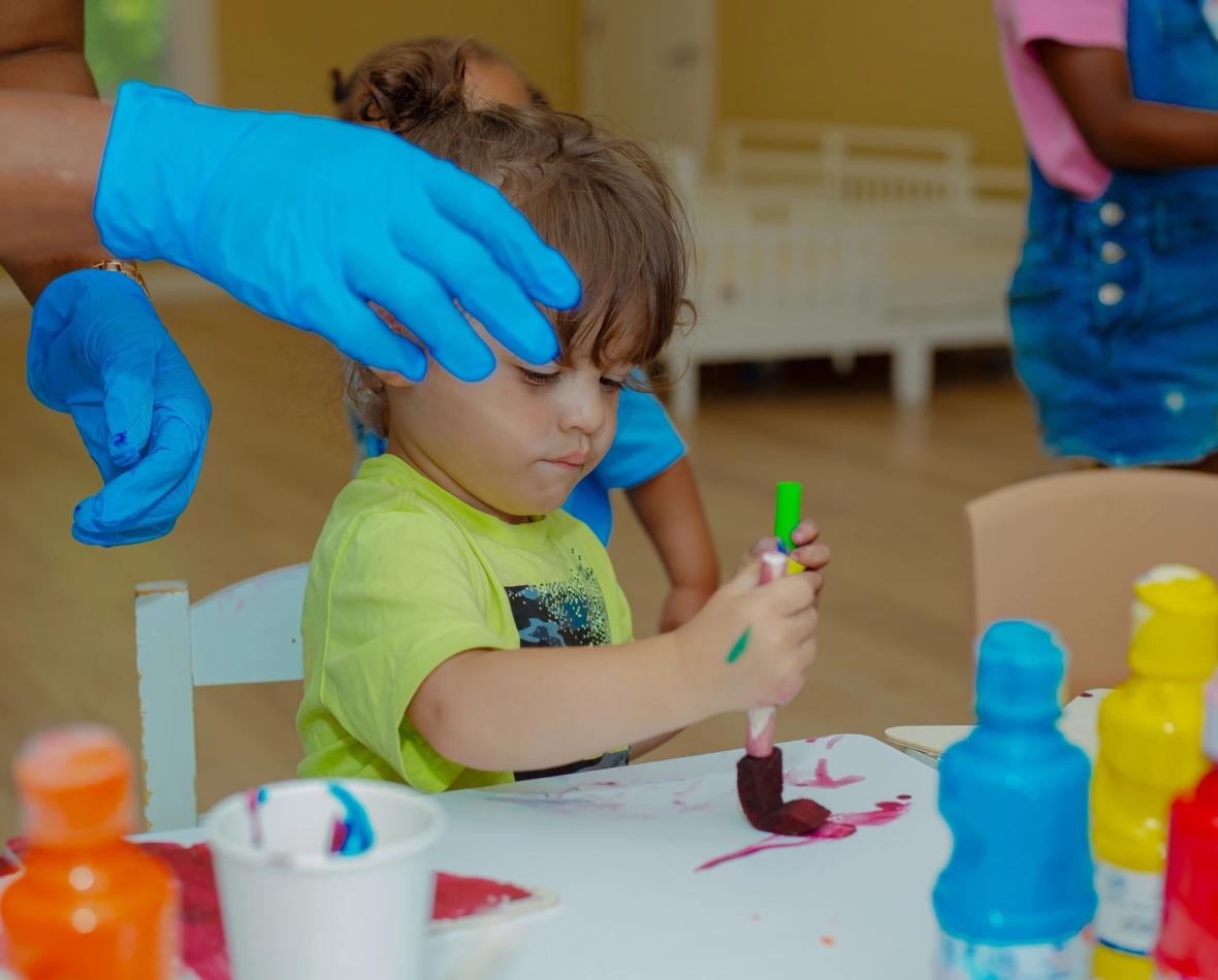 Toddler painting with a teacher nearby