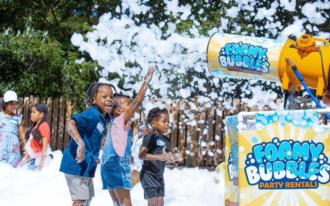 Children reaching toward a foam cannon at a family event