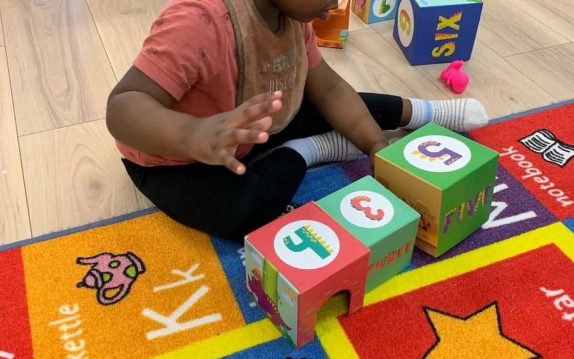 A child stacking alphabet blocks on the classroom rug