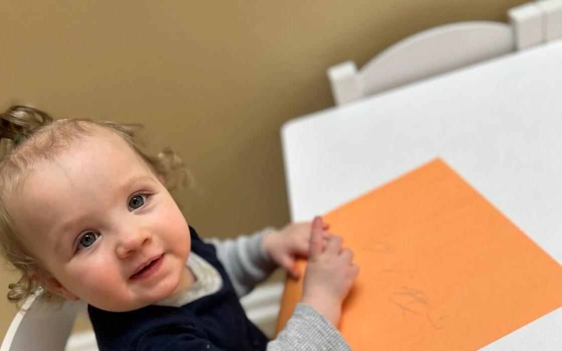 A baby exploring coloured paper at the table